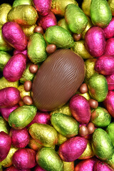 Pile or group of multi colored and different sizes of colourful foil wrapped chocolate easter eggs in pink, red, yellow and lime green with a large brown milk chocolate egg in the middle.