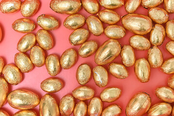 Small pile or group of gold, orange and bronze foil wrapped chocolate easter eggs, against a peach orange background.