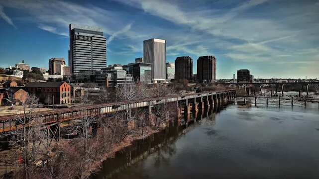 Cinematic aerial view of downtown Richmond Virginia skyline and James River with industrial bridge foreground