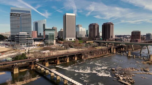Cinematic aerial view of downtown Richmond Virginia skyline and James River with industrial bridge foreground