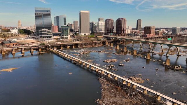 Cinematic aerial view of downtown Richmond Virginia skyline and James River with industrial bridge foreground