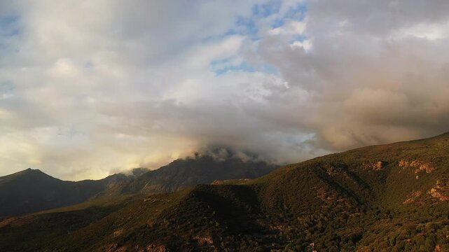 Dramatic clouds over rolling green hills and mountains in the Corsican countryside at sunset, creating a tranquil and atmospheric landscape.