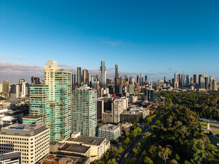 Obraz premium Expansive Aerial View of a Modern Cityscape Dominated by Skyscrapers Bordering Lush Green Parklands Under a Clear Blue Sky.