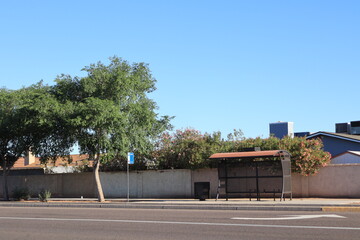 Bright sunny Sunday morning at empty roadside city bus stop with cozy waiting bench and modern shade shelter, Phoenix, Arizona; copy space