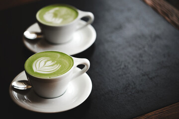 Two cups of matcha latte on black table
