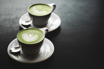 Two cups of matcha latte on black table