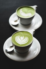 Two cups of matcha latte on black table