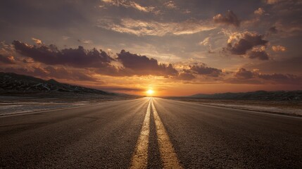 Fototapeta premium A vast asphalt road stretches toward a brilliant sunset, bisecting a desert landscape under a dynamic sky. Sunlight illuminates the path ahead