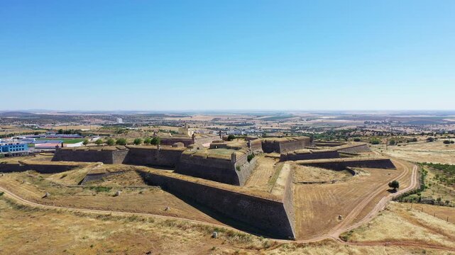 Aerial view of Forte de Santa Luzia, a historic star shaped fortress surrounded by dry landscape in Elvas, Portugal, under a clear blue sky.