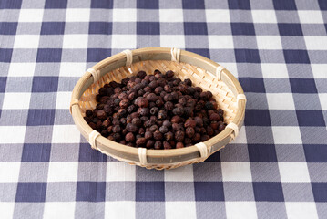 Dried organic hawthorn berries in a bamboo basket on a blue and white checkered tablecloth. Healthy herbal ingredient and wellness concept