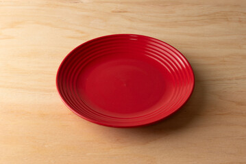 Empty red ceramic plate on a light wooden surface. Minimalist tableware and dining concept for food presentation or copy space