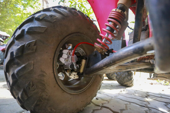 Detailed close up shot of dirty heavy duty black tire, strong red suspension spring and chassis of adventure off road ATV vehicle parked pavement outdoor showing tough vibe ready for extreme