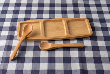 Wooden compartment tray with two spoons on blue and white checkered tablecloth