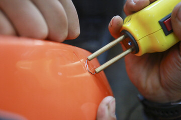 Naklejka premium Concentrated man repairing broken orange plastic part using hot stapler welder tool with careful focus on fixing crack damage professionally in workshop setting