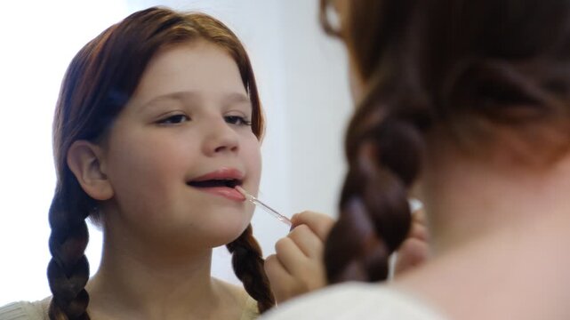 Teenage girl applying lip balm and looking to mirror at home. Makeup, young female applying a treatment. Real life