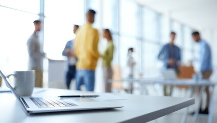 Professional team collaborating in a bright, modern office, with a laptop and coffee cup on the foreground desk, symbolizing contemporary business productivity and teamwork