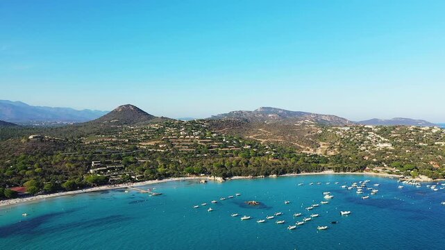 Scenic aerial view of Plage de Santa Giulia with turquoise waters, anchored boats, and lush green hills in Corsica, France.