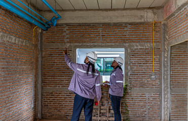 Two Black construction workers in safety helmets review plans on a laptop at a brick building site, highlighting teamwork, technology and workplace diversity in the construction industry. Team work