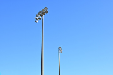 Two towers with stadium light clusters rise against a blue sky