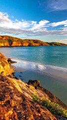 Coastal vista with warm rock formations meeting a serene bay under a partially cloudy sky