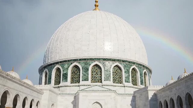 A grand white marble dome of a mosque with intricate green patterns and arched windows, under a sky with a faint rainbow.