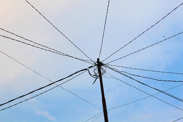Fototapeta premium Messy electrical power lines and cables on a utility pole against clear sky, urban infrastructure development and energy distribution system concept, tangled wire communication network