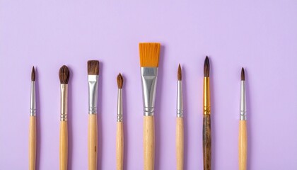 Row of assorted paintbrushes on purple background.
