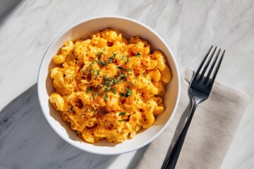 Overhead close-up of creamy, baked macaroni and cheese (mac n cheese) topped with fresh herbs and paprika, served in a white bowl on a bright marble background.