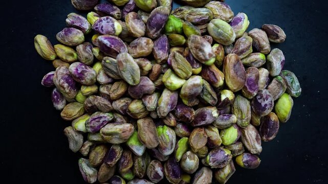 Close-up of unshelled pistachios on a dark surface
