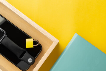 Smartphone with a yellow padlock on its screen placed in a wooden tray on a colorful background. Minimalist digital detox concept representing social media detox and mental wellness.