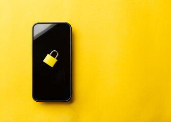 High angle view of a yellow padlock placed on a black smartphone screen over a bright yellow background. Concept of mobile data security, cyber privacy protection, and encrypted digital safety.