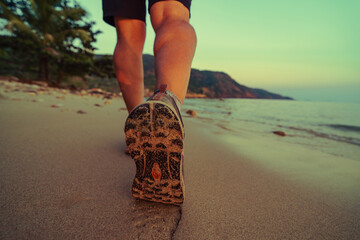 Man walking on sandy beach at sunset, close-up on sport shoes and footprints in sand. The peaceful, tranquil atmosphere, perfect for themes of travel, fitness, vacation, solitude, healthy lifestyle © avtk