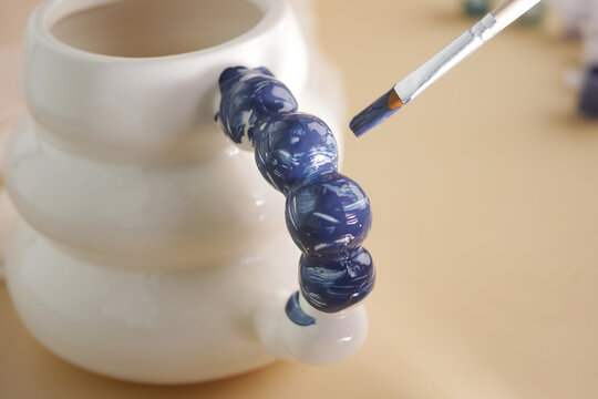 Painting a ceramic piece with blue color and brush - Powered by Adobe