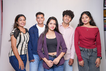 Group of young indian gen z friends standing together on a white background looking at camera.