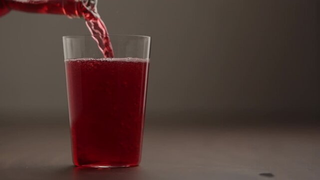 Slow motion pour berry soft drink in tumbler glass on wood table with copy space