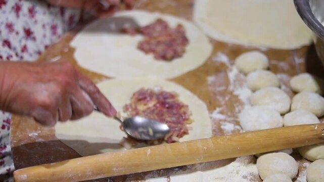 Close-up of an elderly woman's female hands rolling out dough with a wooden rolling pin. Making homemade pies and chebureks.