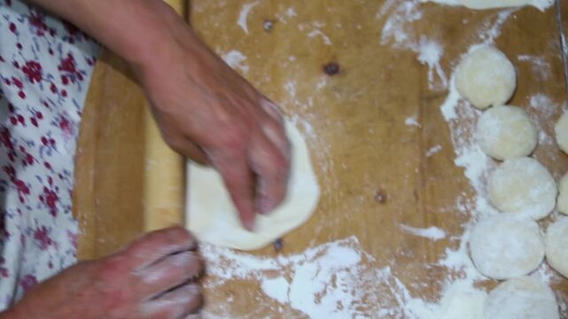 Close-up of an elderly woman's female hands rolling out dough with a wooden rolling pin. Making homemade pies and chebureks.