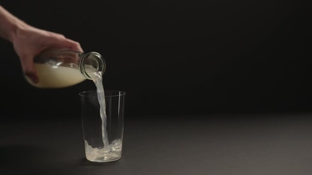 Slow motion man hand pour lemon ginger lemonade into tumbler glass on black paper background with copy space