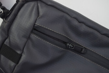 Close-up of a black zipper on a grey textured fabric bag, focusing on the fastener and stitching