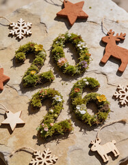 Eco-friendly New Year 2026 flat-lay featuring numbers written with real moss and flowers on textured stone, reusable wooden decorations, earthy tones, sustainable lifestyle concept