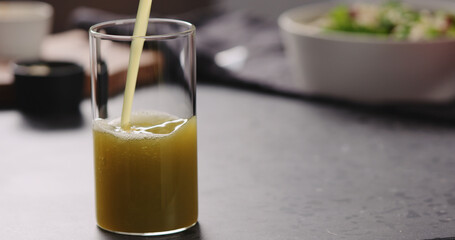 pour apple celery juice in glass on concrete countertop with copy space