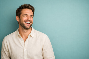 Fototapeta premium Horizontal portrait photo of a laughing man in a light shirt against a teal background, expressing joy, emotional freedom, positive mindset, ideal for happiness, stress relief, mental wellness themes