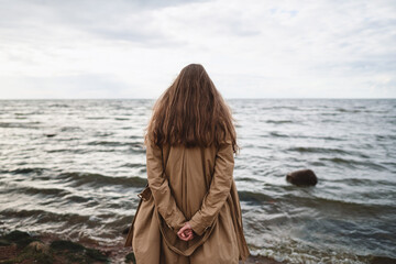 pretty girl walking on a beach in beige trench coat from behind