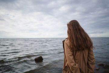 pretty girl walking on a beach in beige trench coat from behind