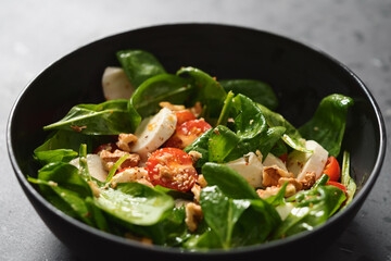 Salad with spinach, tomatoes and mozzarella in black bowl on concrete countertop