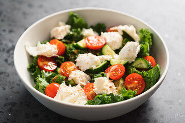 Salad with kale, tomatoes, cucumbers and mozzarella in white bowl