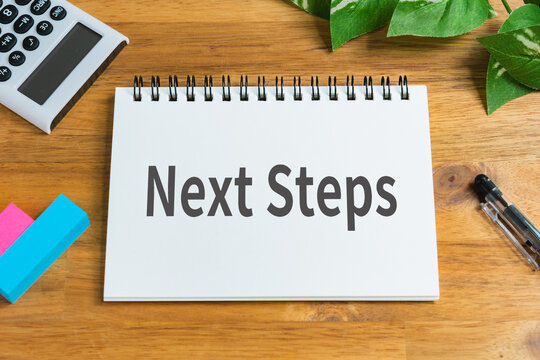Next steps concept on notepad with calculator and green plant on wooden desk