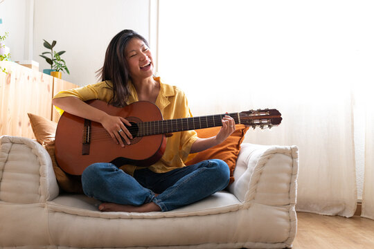 Asian woman playing acoustic guitar and singing at home
