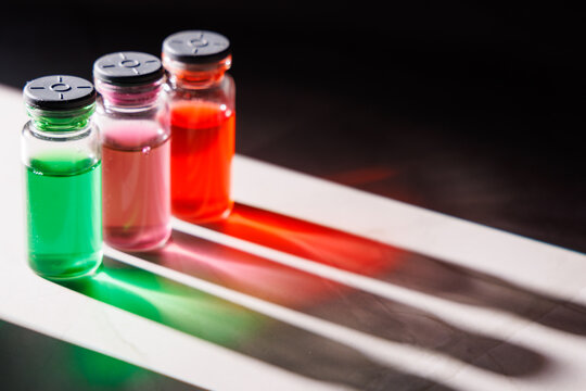 Top view of medical vials with colorful liquids and light reflections on a marble table over black background for biotech themes.