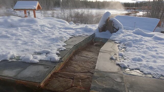 A stationary shot of a stream of warm, iron-rich mineral water flowing through a snow-covered flagstone channel at the nordic hot springs near Whitehorse, Yukon